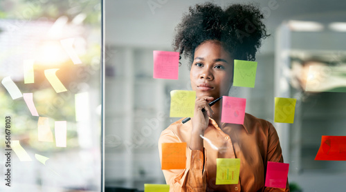 Fotografia Young smiley attractive, businesswoman using sticky notes in glass wall to writi