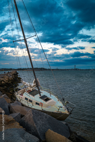 Abandoned sailboat moored at the jetty of Provincetwon Causeway in Cape Cod Bay, Massachusetts, USA, oceanside beach seascape and dramatic cloudscape in Provincetown at twilight