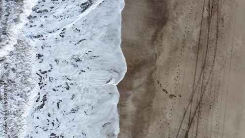 Cenital spiral drone shot of the sea waves breaking on the beach with tracks on the sand, in Cariló, Argentina. photo