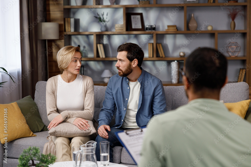 Obraz premium A visit to a family psychologist for a married couple. An African-American psychologist doctor consults an unhappy married couple. Relationship problems in family life. Husband and wife in a quarrel.