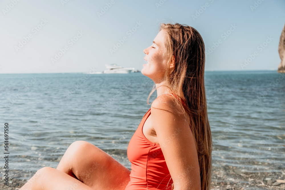 Young woman in red bikini on Beach. Girl lying on pebble beach and enjoying sun. Happy lady with long hair in bathing suit chilling and sunbathing by turquoise sea ocean on hot summer day. Close up