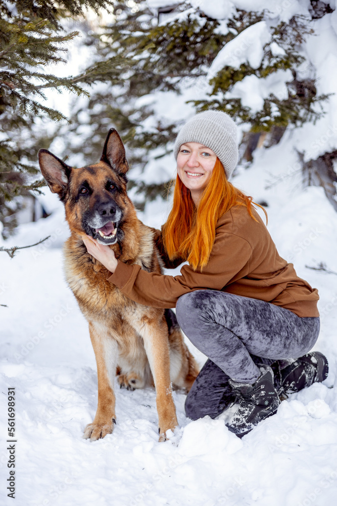 Smiling young woman in enjoying a good day and posing with a pet in the winter forest. Adorable german shepherd dog traveling with young hipster woman