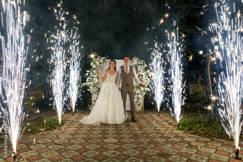 The bride and groom in a wedding dress in the sparks of fireworks at night. photo