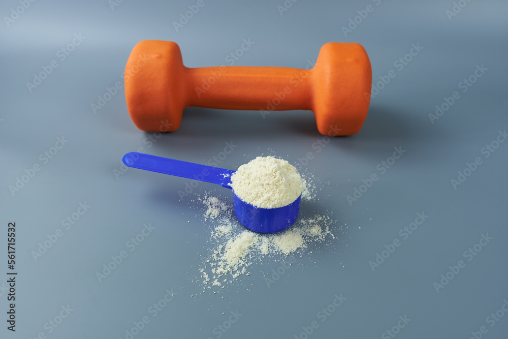 Vanilla whey protein and an orange dumbbell on a gray background. Sports nutrition. Vanilla whey protein and an orange dumbbell on a gray background. Sports nutrition.
