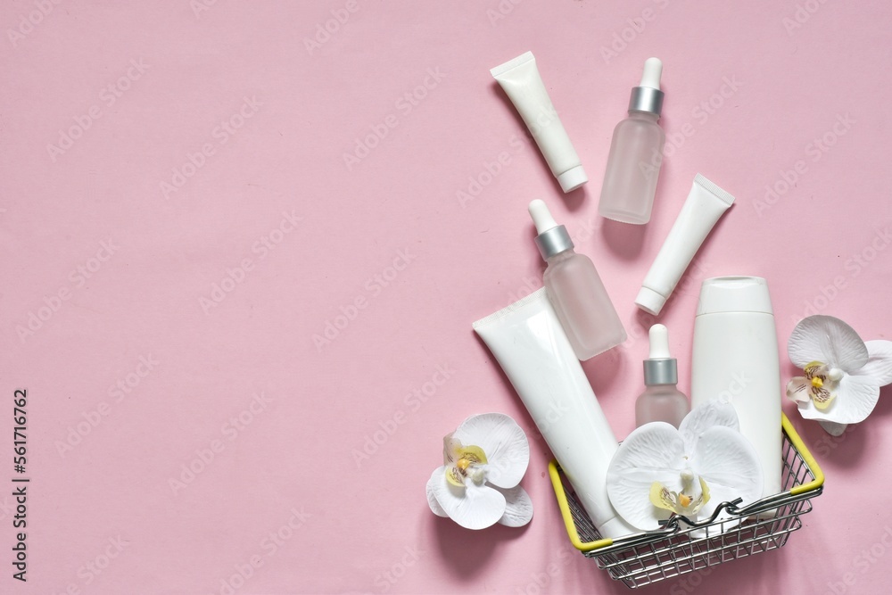 White tubes and bottles with pipettes for cosmetics products in shopping basket on a pink background with orchid flowers. Shopping. Mockup. Copy space. Advertising natural cosmetic. White tubes and bottles with pipettes for cosmetics products in shopping basket on a pink background with orchid flowers. Shopping. Mockup. Copy space. Advertising natural cosmetic.