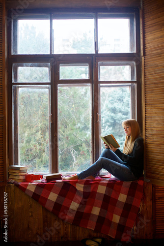 Charming young dreamy girl sits on a window with a book and cup. © Fotoproff