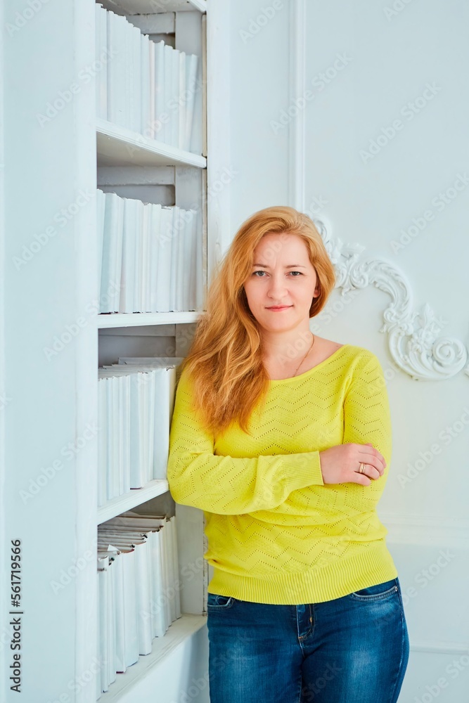 The girl is standing in the loft interior by the bookcase.