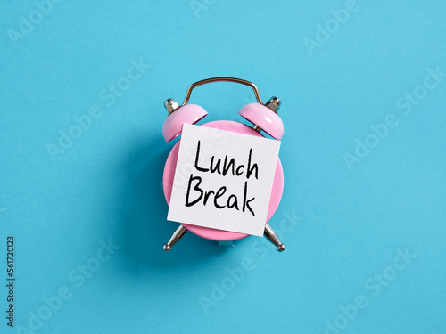Lunch break time reminder or notice message. Pink alarm clock with a note paper on blue background with the message lunch break. photo