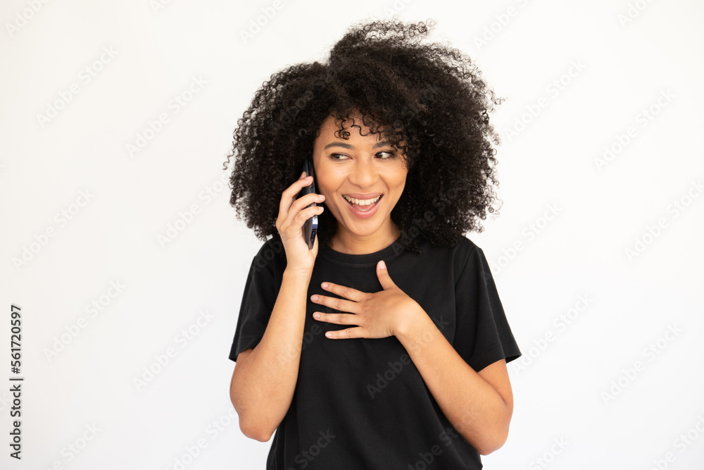 Portrait of happy young woman talking on mobile phone over white background. Biracial lady with afro hairstyle wearing black T-shirt calling friend. Mobile communication concept Portrait of happy young woman talking on mobile phone over white background. Biracial lady with afro hairstyle wearing black T-shirt calling friend. Mobile communication concept
