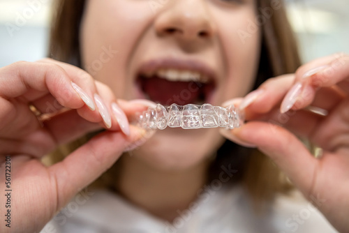 Portrait of beautiful girl patient holding orthodontic retainers aligners in dental clinic.