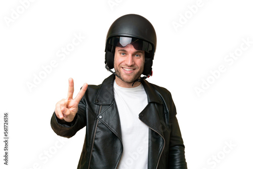 Young caucasian man with a motorcycle helmet isolated on green chroma background smiling and showing victory sign