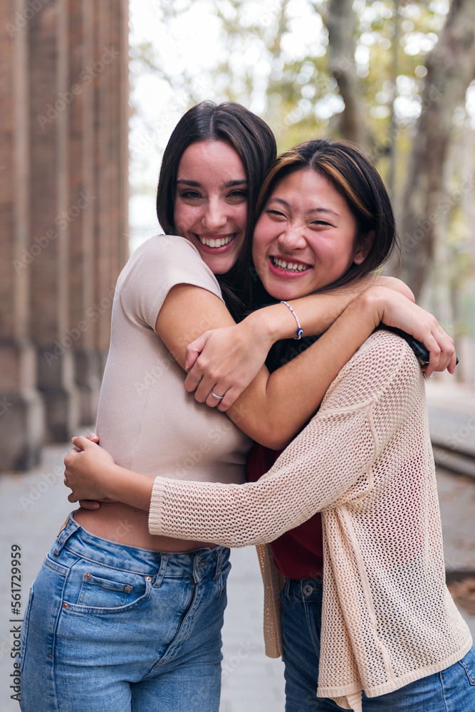 two young women smiling and hugging looking at camera, concept of friendship and love between people of the same sex