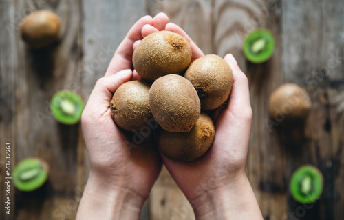Kiwi fruits in female hands on a wooden background, a view of the top.