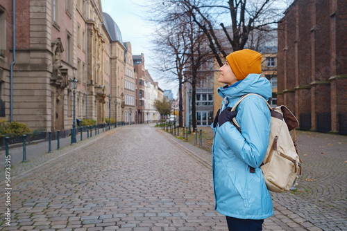 winter travel to Dusseldorf, Germany. young Asian tourist in blue jacket and yellow hat (symbol of Ukraine) walks through sights of old town or Altstadt. Popular center of Rheinland and Westphalia