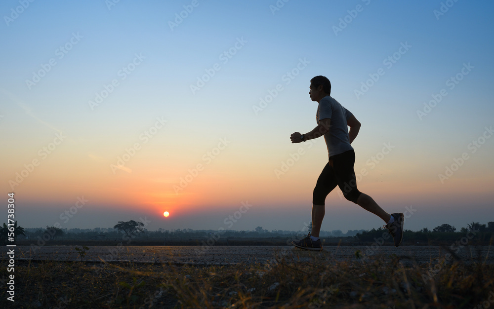 Asain man jogging on country road with sunrise background.
