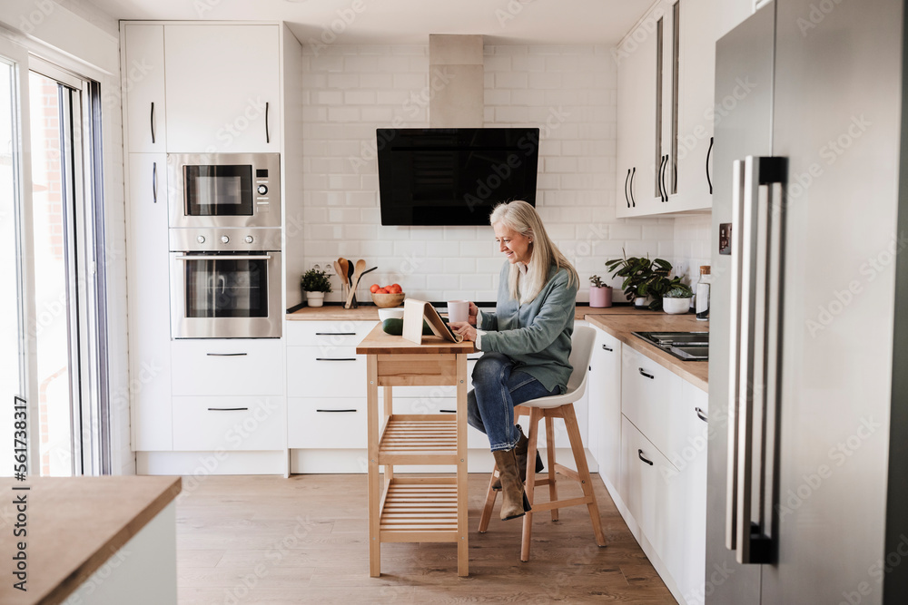 Mature woman using tablet PC sitting in kitchen at home Mature woman using tablet PC sitting in kitchen at home