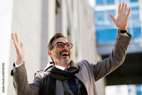 Cheerful mature businessman with hand raised outside office building