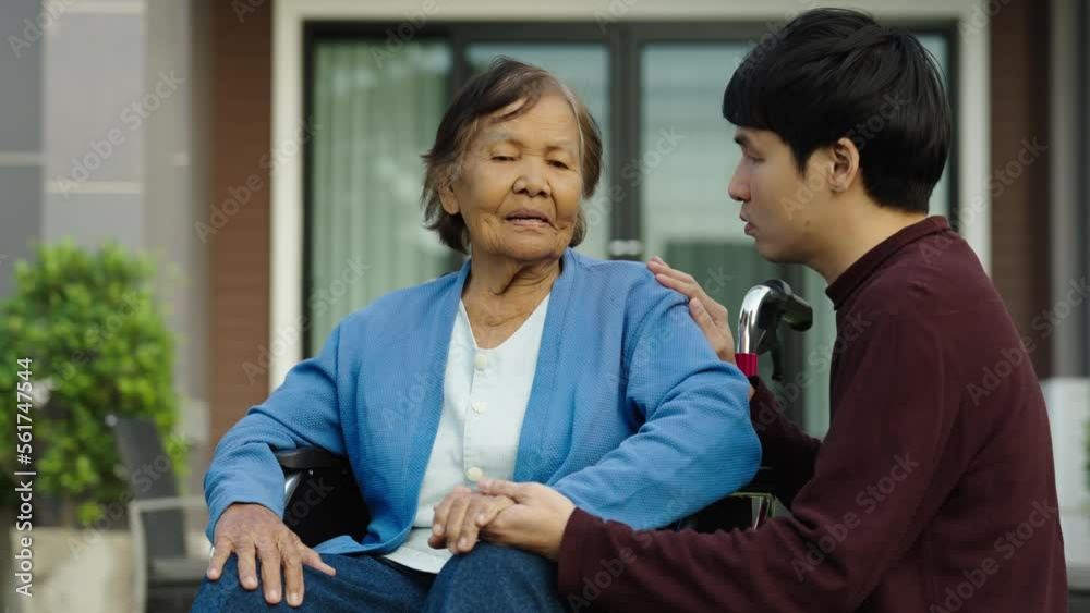 young man grandson take care and holding hand with senior woman sitting in wheelchair at outside the house young man grandson take care and holding hand with senior woman sitting in wheelchair at outside the house