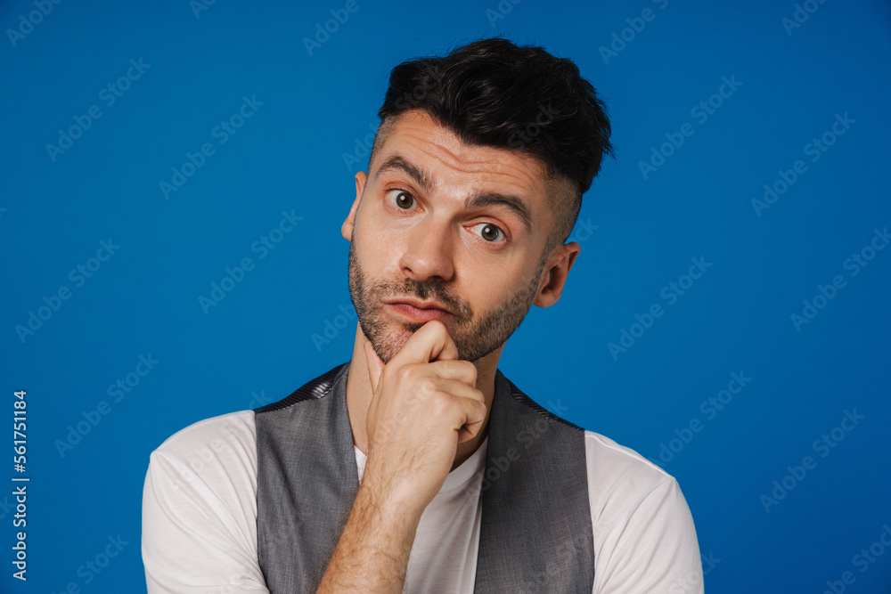 Pensive man touching his chin and looking at camera isolated over blue wall Pensive man touching his chin and looking at camera isolated over blue wall