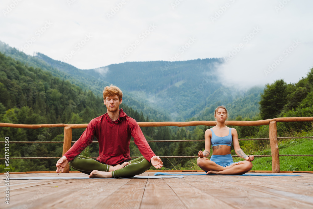 Young white man and woman practicing yoga on fitness mats in forest