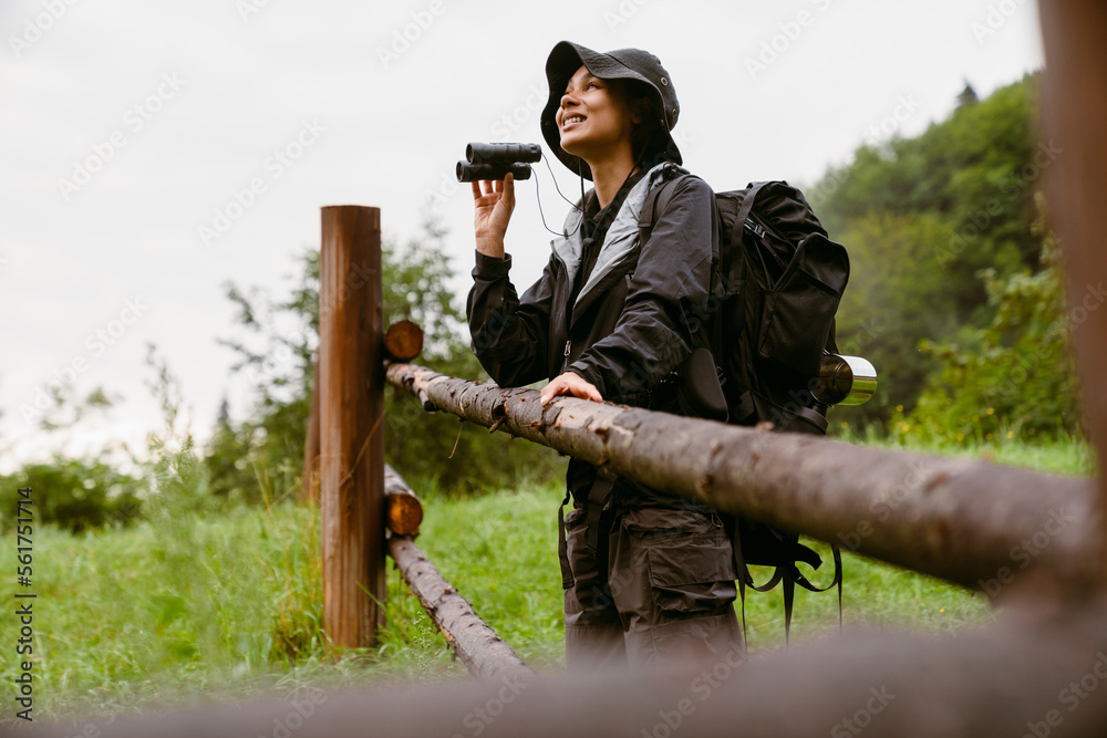 Young white woman using binocular while hiking in mountain forest