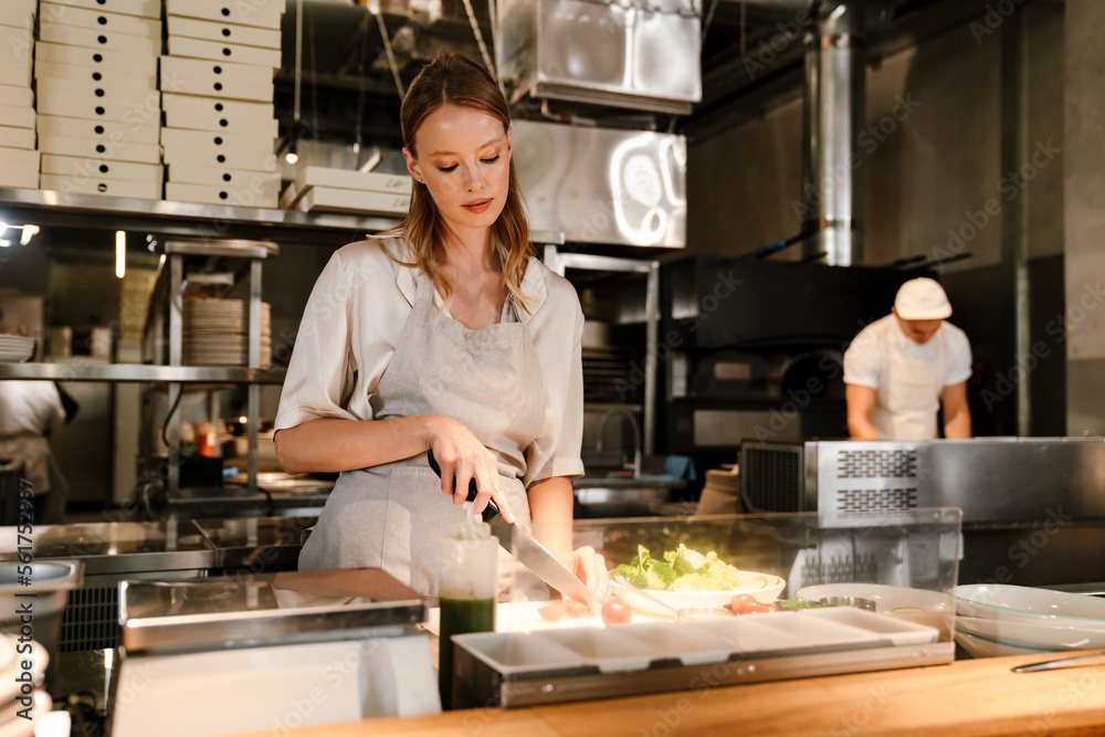 Young white chef woman cooking while working in restaurant kitchen