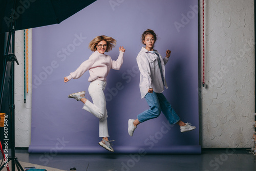 Full legs body size portrait of two positive adorable women jumping isolated on purple background.