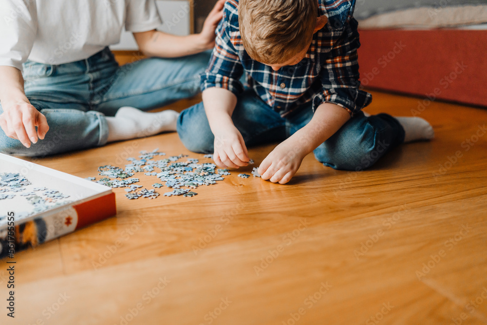 Boy playing with puzzle pieces while sitting with his mom on floor Boy playing with puzzle pieces while sitting with his mom on floor