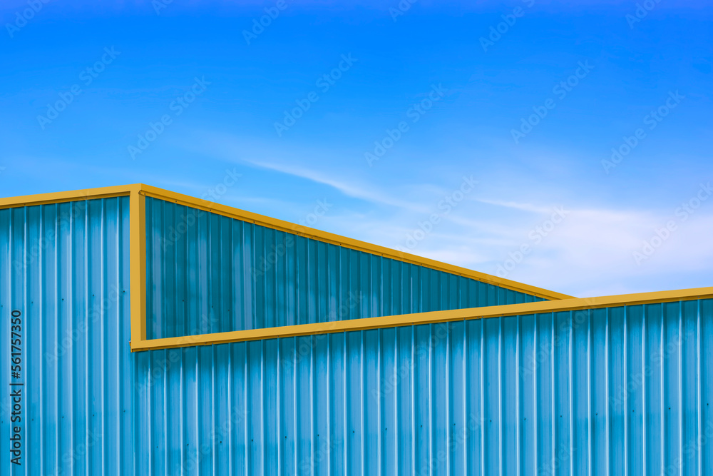 The old blue corrugated metal with yellow edge of warehouse building in industrial style against blue sky background