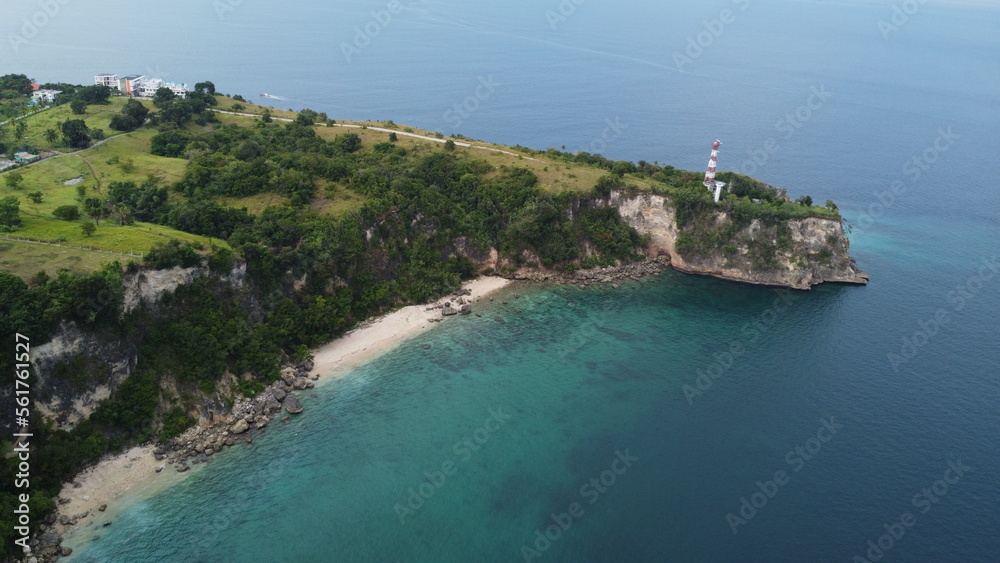 View of the strait. A lighthouse on the edge of a cliff covered with tropical trees.