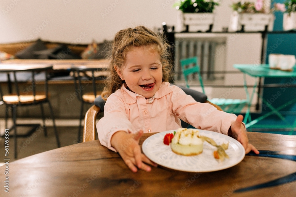 Happy surprised little girl sitting in cafe with healthy desert. The child sits at a table in a cafe and is happy. A happy birthday girl with dessert. Happy surprised little girl sitting in cafe with healthy desert. The child sits at a table in a cafe and is happy. A happy birthday girl with dessert.