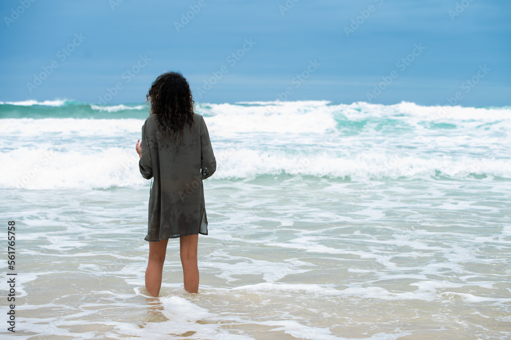 Woman seen standing in water as waves rush in