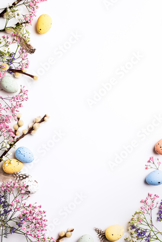Border with Easter composition with spring flowers and colorful quail eggs over white background. Springtime and Easter holiday concept with copy space. Top view