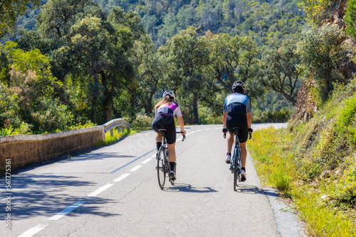 Couple of cyclist ride together on road bicycles in beautiful nature.
