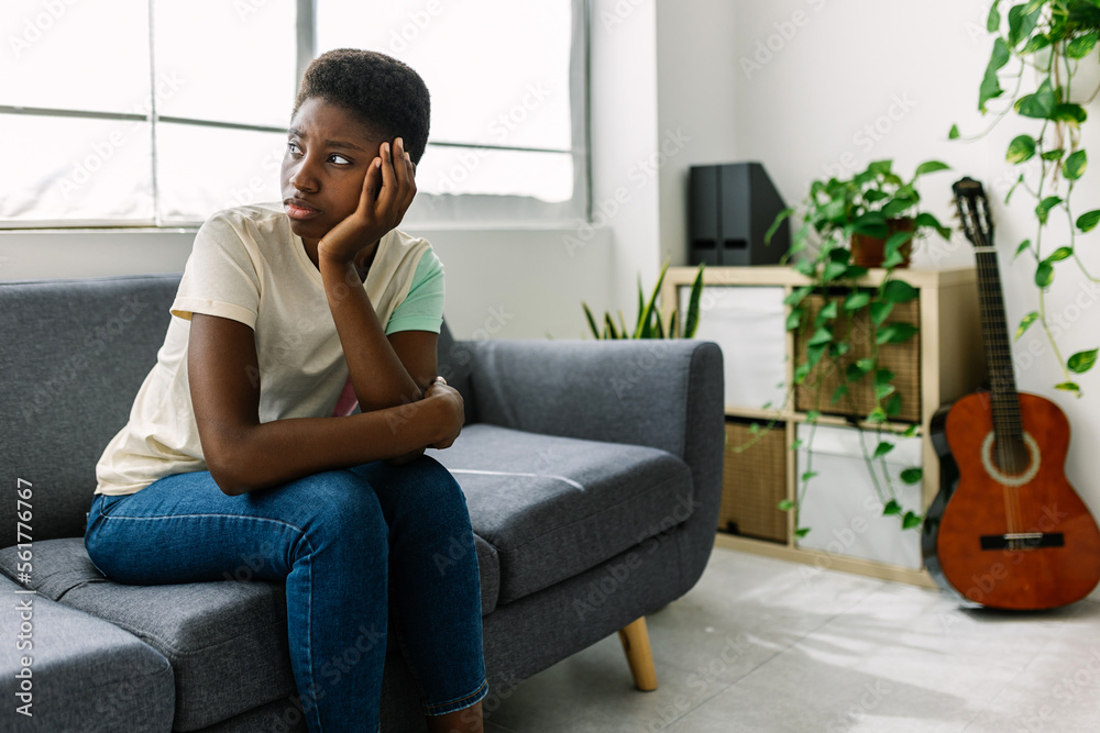 Young black woman sitting on sofa in the living room feeling worried thinking about personal problems Young black woman sitting on sofa in the living room feeling worried thinking about personal problems