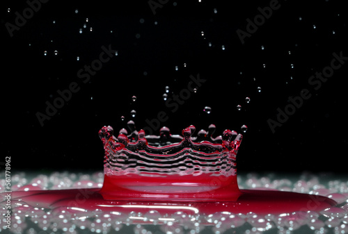 A drop of red water forming a coronet as it splashes into a shallow layer of liquid photo