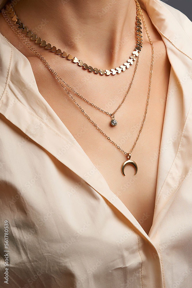 Φωτογραφία Cropped close-up portrait of a woman, demonstrating gold necklaces with pendants in a beige shirt