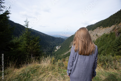 the back of the girl looking at the green mountains. a woman with loose hair stands in the mountains.
