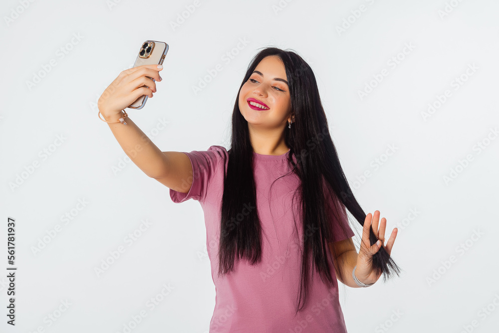Lovely young woman holding smartphone using mobile phone app for video call or selfie photo, standing against white studio background
