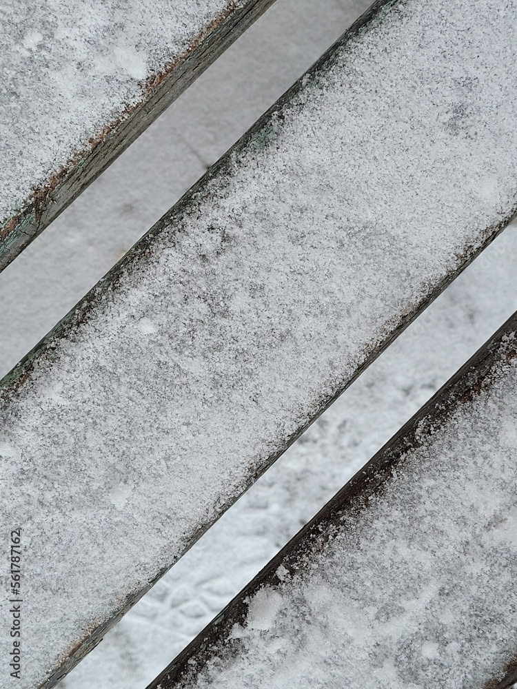 Fototapeta premium Close up of wooden rustic bench in the snow with copy space. First snow. Winter is coming concept. Creative diagonal line background. Website banner.