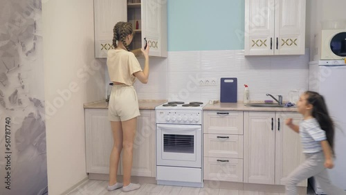 A beautiful Caucasian girl is having fun and dancing with her little daughter in the kitchen of the house. The daughter runs towards her mother.Happy family having fun, listening to music. Childhood