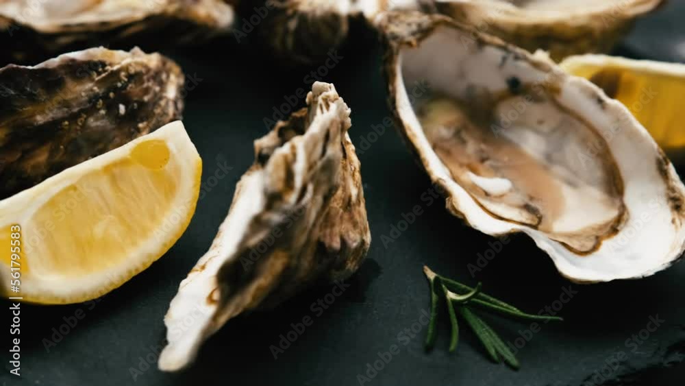 Fresh oysters with lemon spinning on black round platter. Closeup view of seafood Fresh oysters with lemon spinning on black round platter. Closeup view of seafood