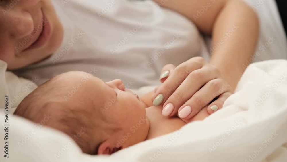 Beautiful young mother lying in the bed and looking at sleeping newborn baby. Adorable infant child napping with his mom at home. Girl strocking tiny hand of cute resting little kid Beautiful young mother lying in the bed and looking at sleeping newborn baby. Adorable infant child napping with his mom at home. Girl strocking tiny hand of cute resting little kid