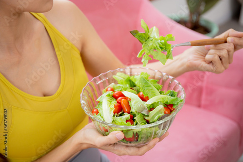 Closeup hands of woman holding salad vegetable in bowl and eating lettuce in living room at home, female satisfied and vegetarian food for healthy and nutrition, lifestyles and health concept.