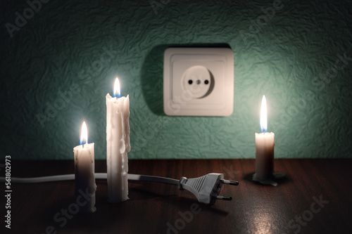 A burning candle next to an outlet and an electric plug. Blackout, power outage, energy crisis or power outages, conceptual image. Ukraine, the lack of light due to an accident at an electric power photo