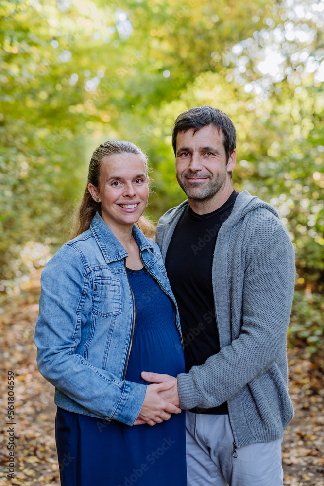 Obraz premium Portrait of happy pregnant woman and her husband, standing in forest.
