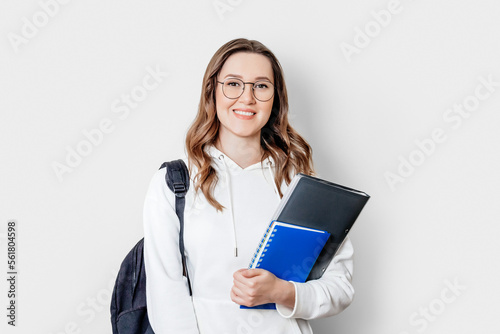 a girl student in glasses and a hoodie holds books smiling on a white background