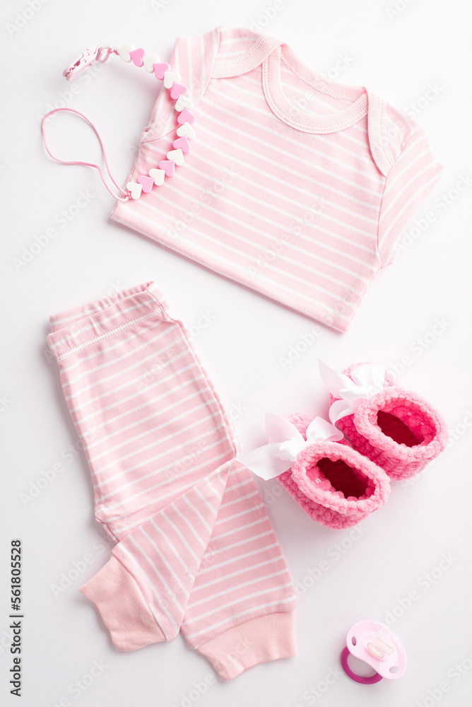 Baby shower concept. Top view vertical photo of pink shirt pants knitted shoes dummy and teether chain on isolated white background Baby shower concept. Top view vertical photo of pink shirt pants knitted shoes dummy and teether chain on isolated white background