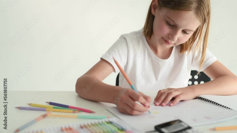Cute child girl drawing with crayons on white paper sitting at table. Person kid painting with colorful pencils Cute child girl drawing with crayons on white paper sitting at table. Person kid painting with colorful pencils