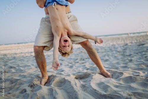 Photography Father holding his son upside down, enjoying summer vacation, having fun